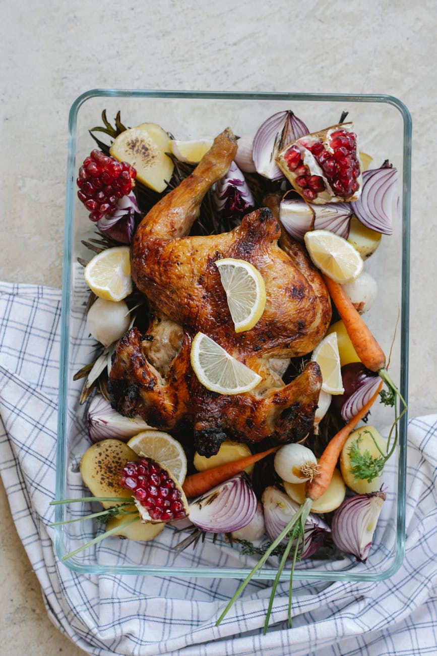 grilled whole chicken with vegetables and fruits in glass bowl.
roasting chicken in a glass bowl