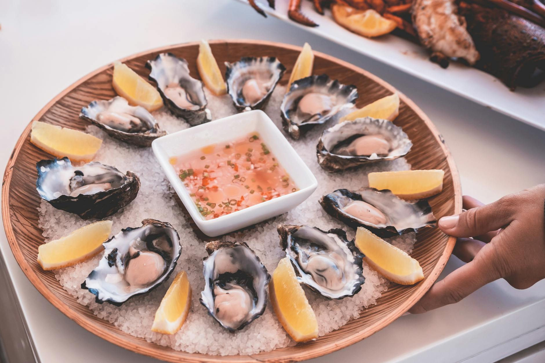anonymous person serving plate of fresh oysters with sauce and lemons on table, Australia day things to do
