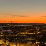 unset view over Lisbon from Miradouro da Senhora do Monte, with red rooftops and the Tagus River in the distance.