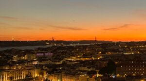Sunset view over Lisbon from Miradouro da Senhora do Monte, with red rooftops and the Tagus River in the distance.