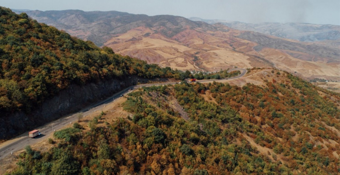 A quiet mountain pass in the Armenian highlands, with a winding road cutting through muted volcanic slopes under an open, pale sky.