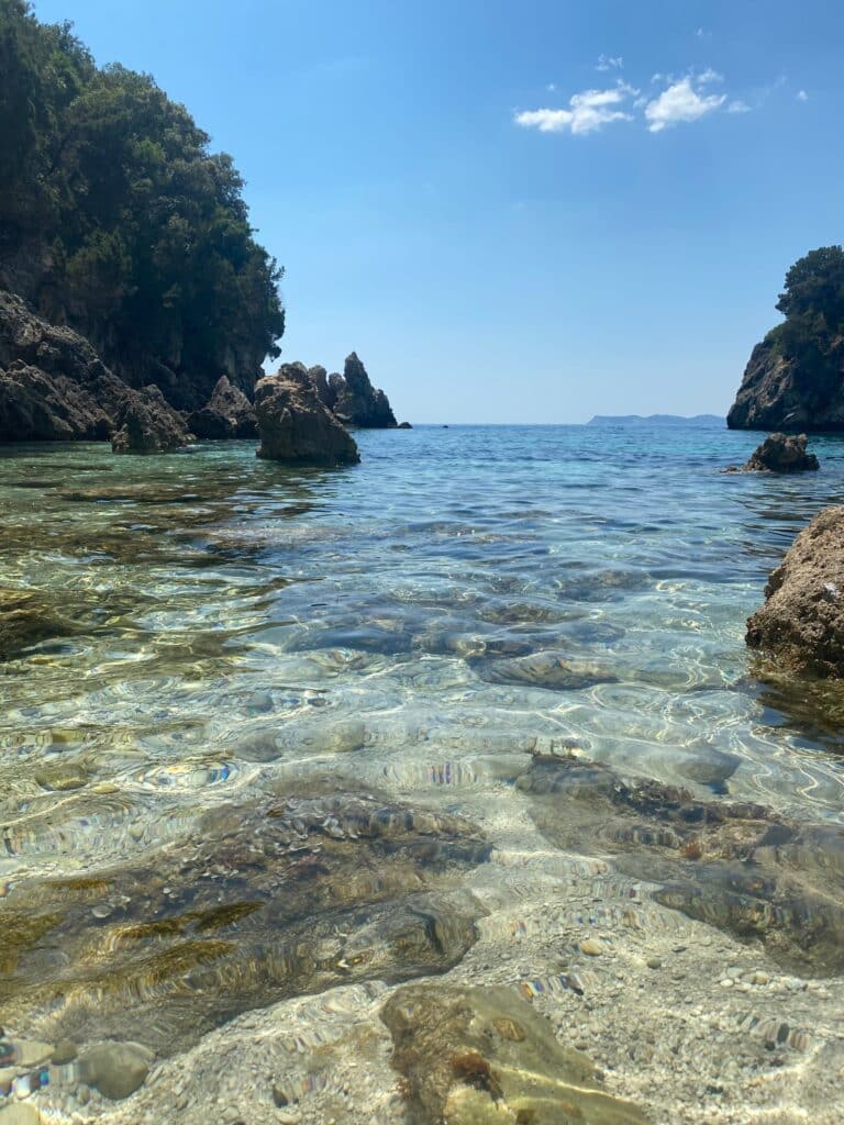 Still coastal cove with glass‑clear water and rocky edges under soft daylight.