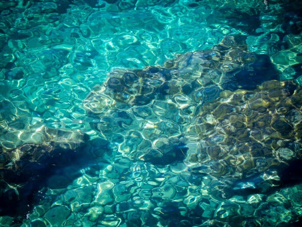 Crystal‑clear turquoise water revealing vibrant coral patches lit by strong noon sunlight.