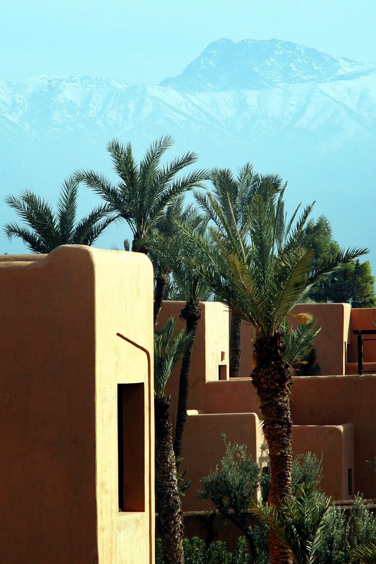 Earth‑toned Marrakesh architecture with the Atlas Mountains in the background, capturing terracotta warmth and the palette shift from Nordic cool to North African light.