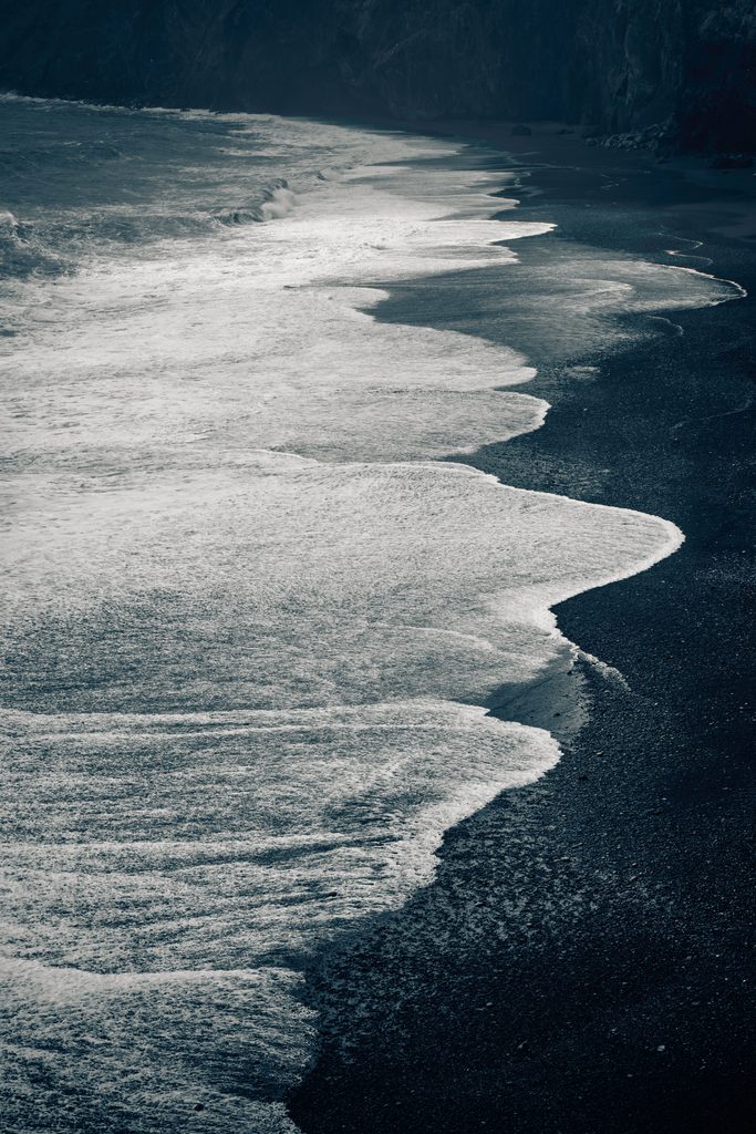 A dramatic Iceland black sand beach with waves breaking against volcanic coastline in early autumn light.
