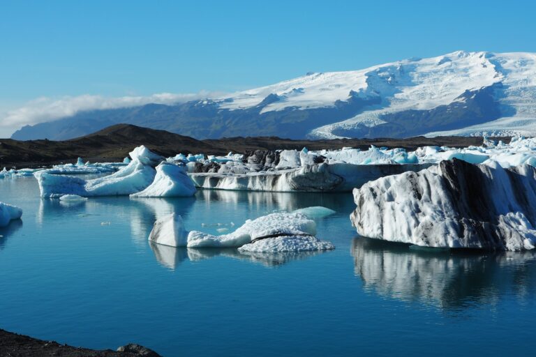 A calm Iceland glacier lagoon with floating icebergs and soft blue reflections in early autumn light.