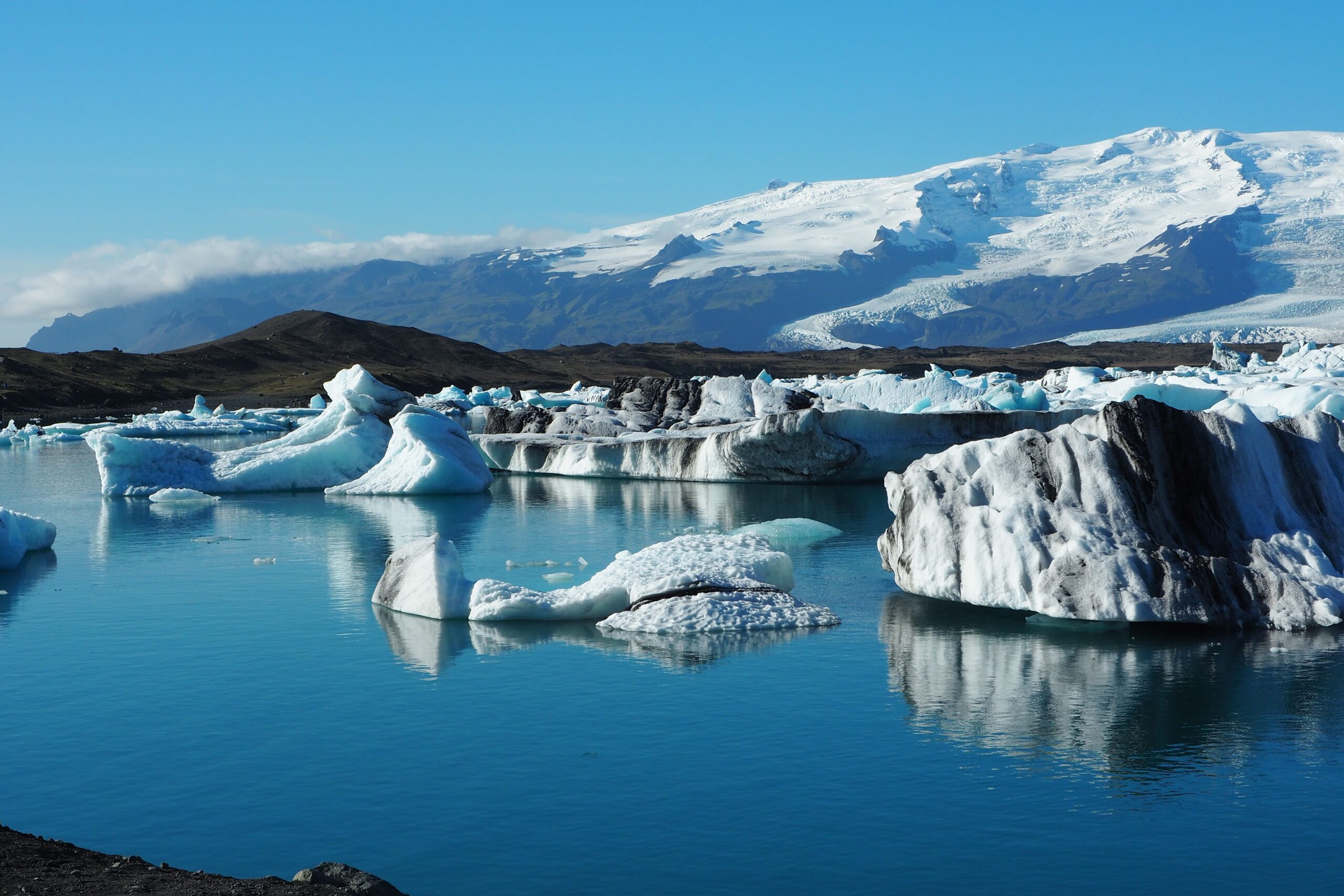 A calm Iceland glacier lagoon with floating icebergs and soft blue reflections in early autumn light.