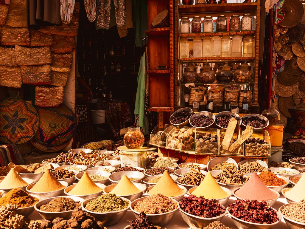 Brass bowls filled with layered Moroccan spices in a sunlit market, showing the complexity of Ras el Hanout.
