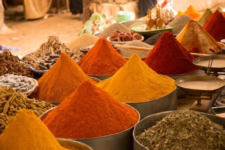 Terracotta‑toned Moroccan spice pyramids with orange and red powders in a Marrakech street market.