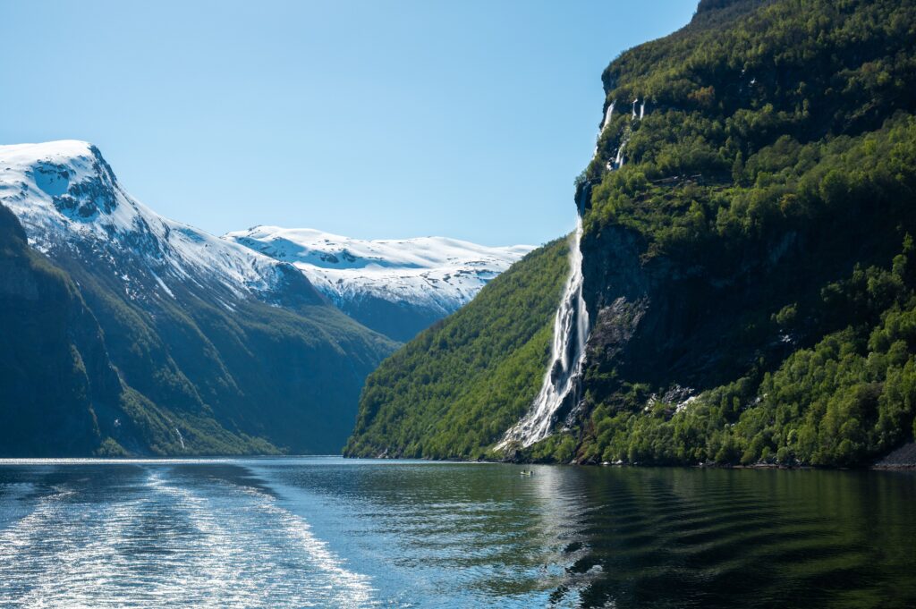 A small boat moving through a deep blue Norwegian fjord surrounded by steep cliffs and mist, capturing Nordic serenity and quiet mountain stillness.
