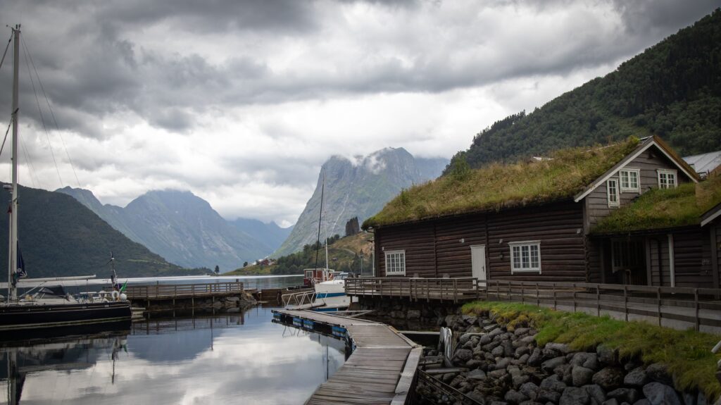 Traditional Norwegian cabins along a calm fjord with misty blue water and steep mountains, reflecting Nordic serenity and quiet mountain stillness.