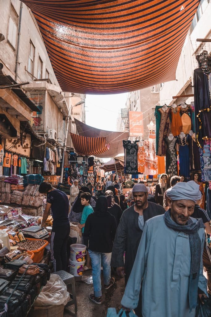 People walking through a busy Cairo market street lined with shops and traditional architecture in Egypt.