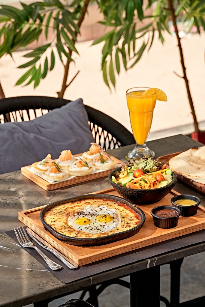 Traditional Egyptian breakfast spread featuring ful medames, bread, vegetables, herbs, and shared breakfast dishes.