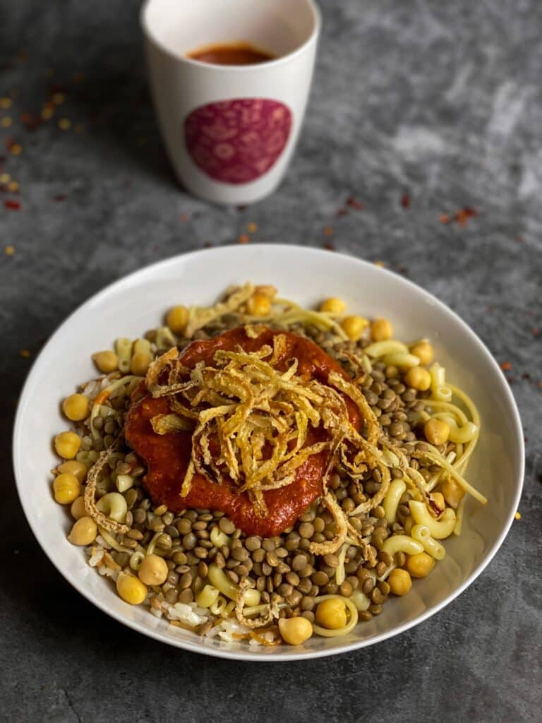 Traditional Egyptian koshari topped with crispy onions, chickpeas, lentils, rice, and tomato sauce.