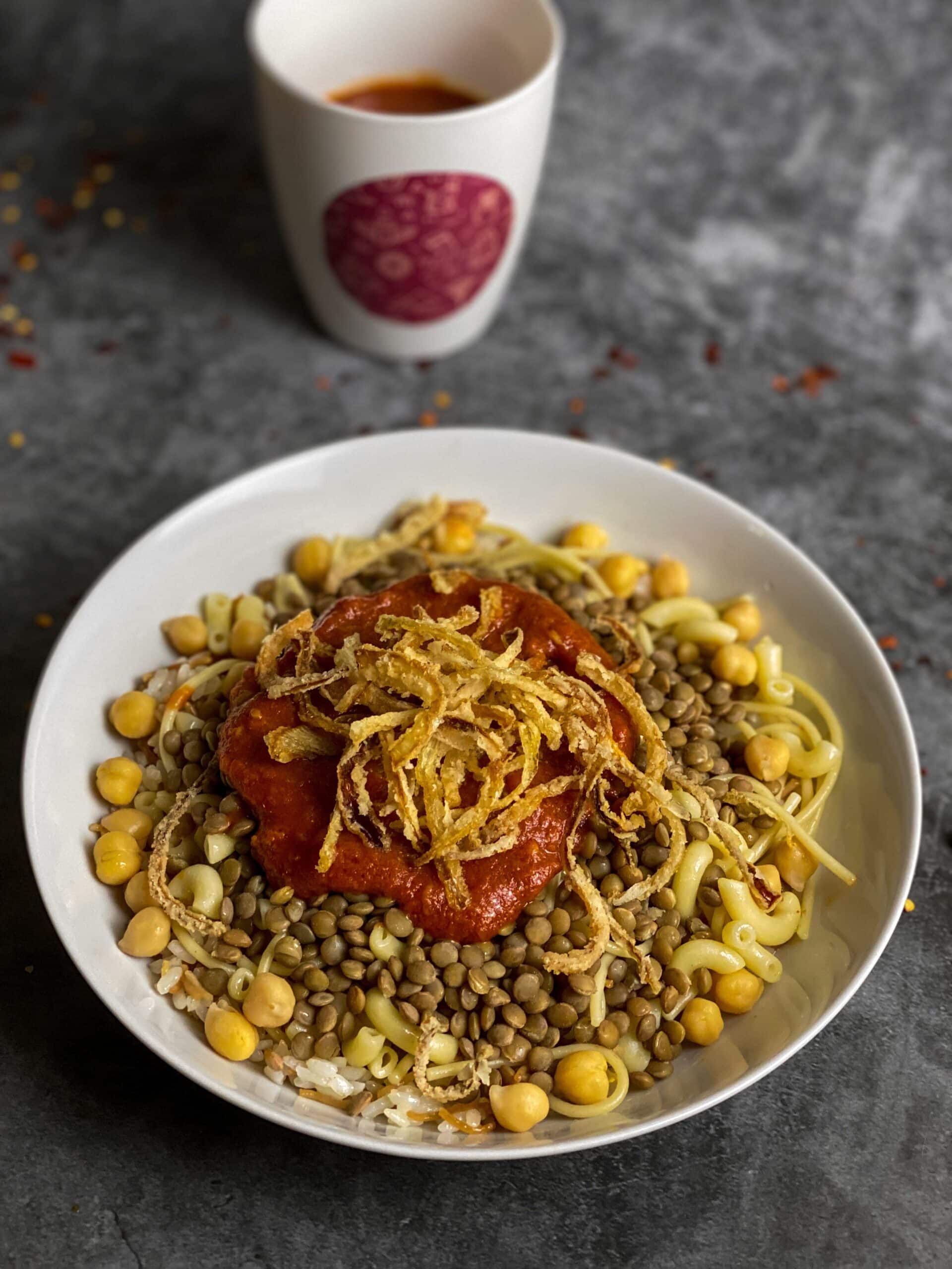 Traditional Egyptian koshari topped with crispy onions, chickpeas, lentils, rice, and tomato sauce.