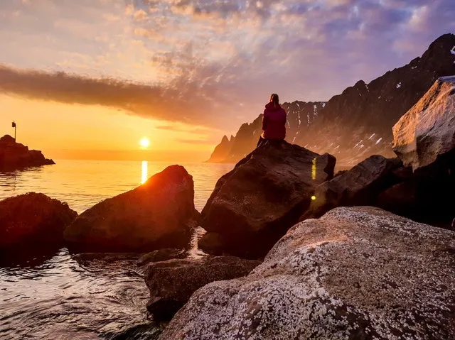 person sitting on rock formation beside body of water European